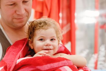 Father holding cute little toddler girl wrapped in towel...