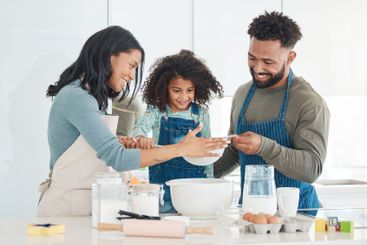 Parents, daughter and flour for baking in kitchen with...