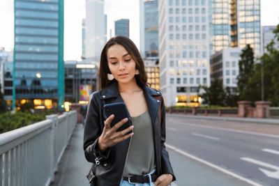 Serious young woman walking outdoors by street in city...
