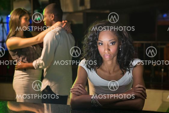 Unhappy woman sitting at bar counter and couple dancing...