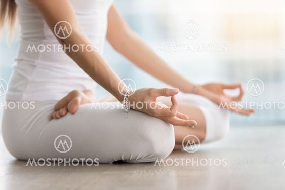 Woman in Padmasana pose with mudra against floor window, closeup