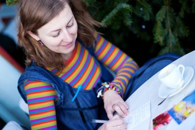 Beautiful girl in bright clothes writing postcards in cafe
