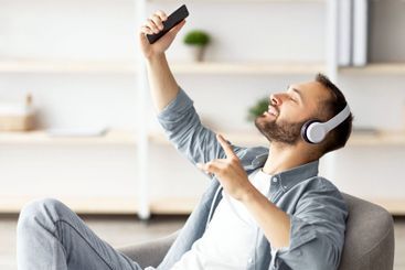 Smiling young Caucasian guy in headphones listening to...