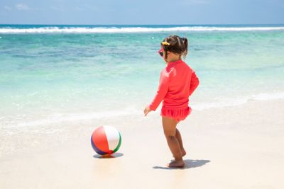 Toddler Girl Playing With Ball Near The Seashore On Beach