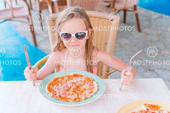 Portrait of cute little girl sitting by dinner table and...
