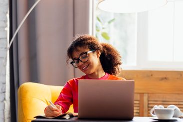 Smiling young African woman is writing in notebook at...