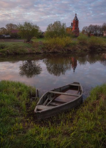 At dusk at the coast in the green grass is a wooden boat.
