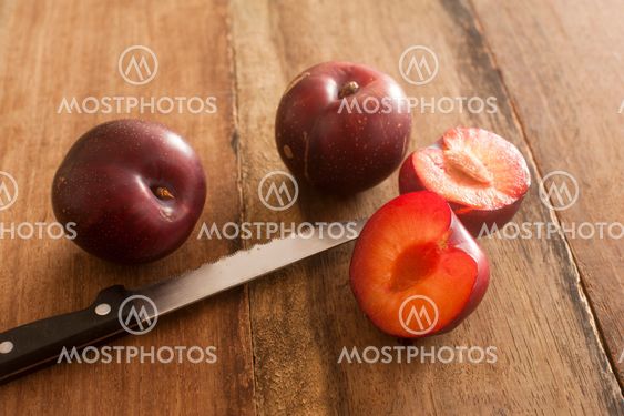 Whole and cut plums with knife on table