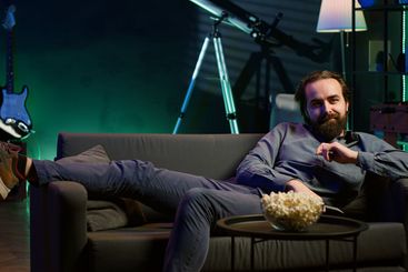 Excited man jumping on couch at home, rushing to watch...