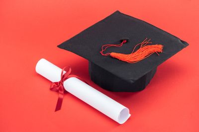 Academic cap with tassel and diploma with ribbon on red...