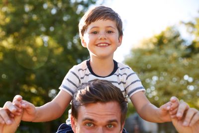 Close Up Of Father Giving Son Ride On Shoulders In Garden...