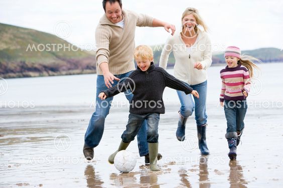 Family playing soccer at beach smiling