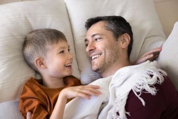 Laughing dad and little son lying on pillows, close up