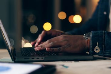 Black man, laptop and working at night in office with...